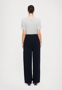 Camiseta gris de manga corta combinada con pantalones de pierna ancha de color marino, con una cintura alta y textura suave, vista desde la parte posterior.
