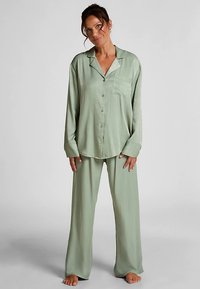 Ensemble de pyjama en satin vert clair comprenant une chemise à boutons avec une poche poitrine et des manches longues, associée à un pantalon large et ample.