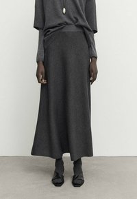 Jupe grise longue avec une finition texturée, associée à un haut ample assorti. Des chaussures noires à bout carré accentuent la tenue.