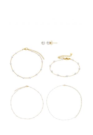 Feine goldene und silberne Kettenhalsketten und Armbänder, verziert mit kleinen weißen Perlen, sowie passende Perlen-Ohrstecker auf weißem Hintergrund.