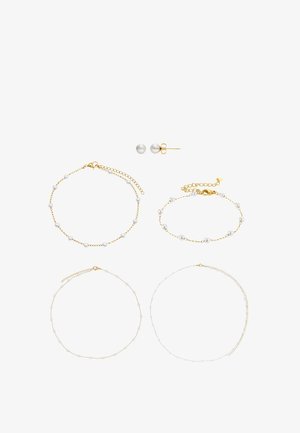 Colliers et bracelets délicats en chaîne d'or et d'argent ornés de petites perles blanches, ainsi que des boucles d'oreilles clous en perles assorties sur fond blanc.
