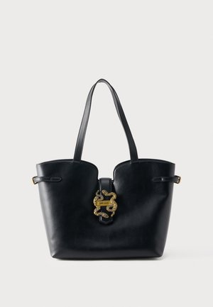 Μαύρη τσάντα tote από δέρμα με διπλές λαβές και χρυσό διακοσμητικό έμβλημα φίδι στο κούμπωμα στο κέντρο μπροστά.