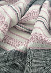 Textiel met geweven patronen in roze, wit en zwart. Het oppervlak heeft een gestructureerd uiterlijk met afwisselend strepen en geometrische motieven.