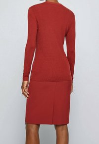 Pull côtelé marron avec manches longues et boutons décoratifs aux poignets, associé à une jupe ajustée assortie marron avec une fente au dos.