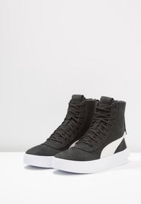 Svarta högsneakers av mocka, med en vit sidodetalj, runt tå, tjock vit sula och knutna snörningar.