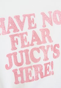 T-shirt blanche avec un texte en paillettes roses brillantes disant "N'AIE PAS PEUR, JUICY EST LÀ !" en police audacieuse et stylisée.