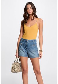 Yellow ribbed bodysuit with thin straps paired with light blue denim shorts featuring two front pockets and silver hardware. Carrying a snake-print handbag.