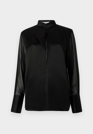 Blouse noire avec un col montant, longues manches transparentes, détail de nœud au cou, en tissu satin lisse, fermeture par boutons sur le devant.