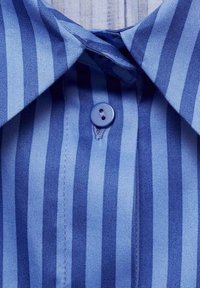 Gros plan du col d'une chemise bleue avec des rayures verticales claires et foncées et un seul bouton bleu fermé au centre devant.