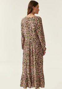 Blumenkleid mit langen Ärmeln in Schwarz mit pinken und grünen Mustern, gerafftem Taillenbereich und gestuftem Volantrock. Glatte Stoffstruktur, runder Ausschnitt.