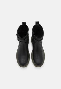 Czarne skórzane botki za kostkę z okrągłym noskiem, z akcentem w postaci klamry z boku i kontrastującą zieloną gumową podeszwą.