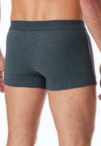 Bóxer masculino gris oscuro, hecho de una tela suave, con un diseño ajustado y una franja blanca en contraste a lo largo de los lados.