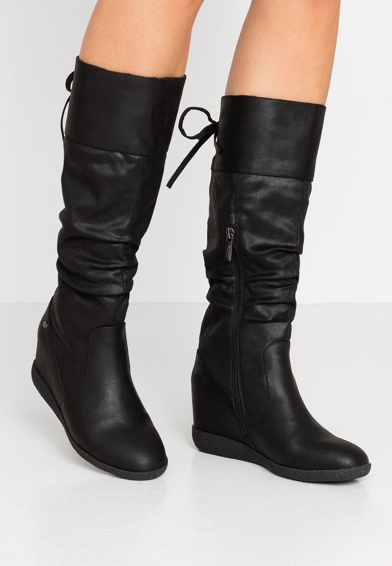Bottes montantes en cuir noir avec un design décontracté, talon compensé, fermeture éclair latérale et accents noués en haut. Semelle texturée pour une meilleure adhérence.