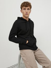 Zwarte rits-hoodie gemaakt van een katoenmix, met een voorkant rits, een trekkoordkap en kangoeroe zakken, gecombineerd met beige broek.