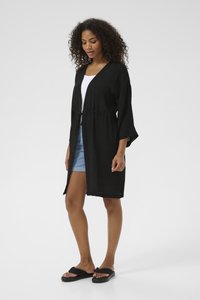 Svart lättviktskimono-stil cardigan med öppen front, vida ärmar, cinchad midja och naturlig textur, tillsammans med jeansshorts och sandaler.