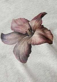 Un tessuto grigio presenta un grande motivo floreale realistico con petali in sfumature di viola e rosa, che mette in mostra texture dettagliate e sottili variazioni di colore.