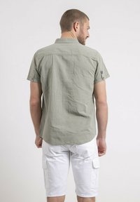 Chemise à manches courtes, de couleur vert clair, avec une coupe décontractée, dotée d'un col boutonné et de manches retroussées, associée à un short cargo blanc.