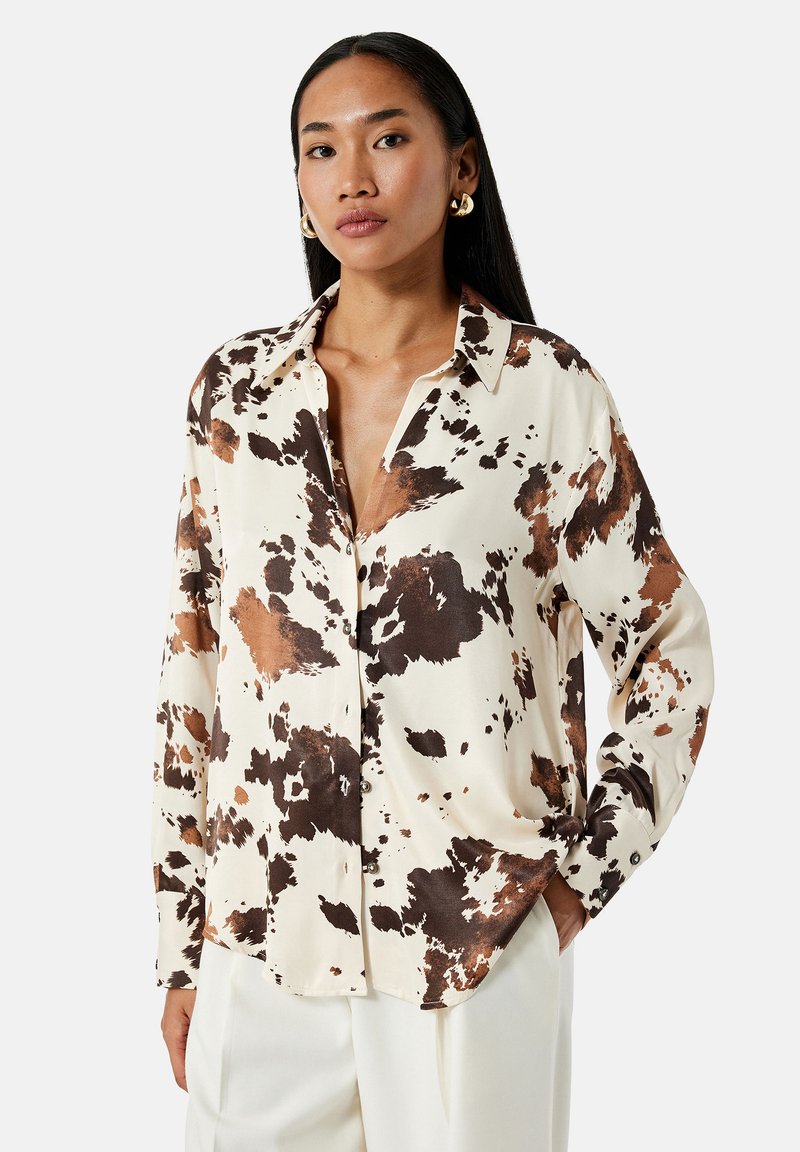 Beige overhemd met grote bruine en zwarte vlekken, voorzien van een knoopsluiting aan de voorkant en een relaxte pasvorm. Glad stoffen textuur.