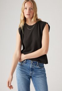 Svart ärmlös t-shirt i mjuk bomull med rund halsringning. I kombination med ljusblå högmidjade jeans som har en klassisk denim-textur.