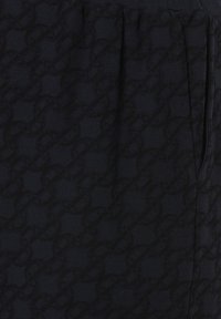 Tela negra con un patrón texturizado que presenta enlaces circulares interconectados. El diseño es sutil, con un acabado suave y un detalle de fruncido.