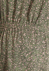 O tecido com estampado floral apresenta folhas verdes e flores sobre um fundo rosa suave. O material tem uma leve textura com detalhes franzidos.