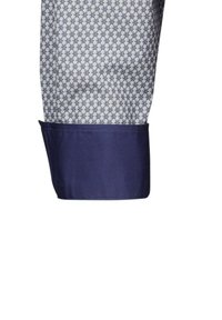 Polsino della camicia blu con un motivo geometrico in blu navy e blu chiaro, con una fascia solida blu navy al polso.