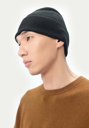 Bonnet en tricot côtelé noir porté par une personne. Le bonnet a un ajustement près de la tête et un sommet arrondi. L'arrière-plan est neutre.