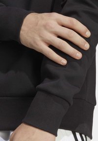 Black sweatshirt featuring ribbed cuffs and hem, soft texture, fitted design, with hand resting on the sleeve for a close-up view.