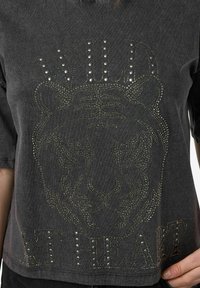 Szara koszulka z krótkim rękawem z graphicznym motywem tygrysa ozdobionym ćwiekami oraz napisem "WILD AT HEART" w metalicznych akcentach. Miękka tkanina w luźnym kroju.