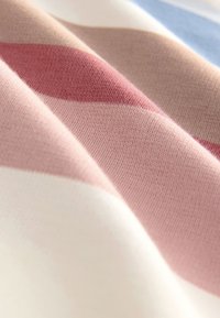 Tessuto a righe con texture morbide nei toni del rosa, bianco e blu, che presenta motivi intrecciati e lisci. La luce si riflette delicatamente sulla superficie.