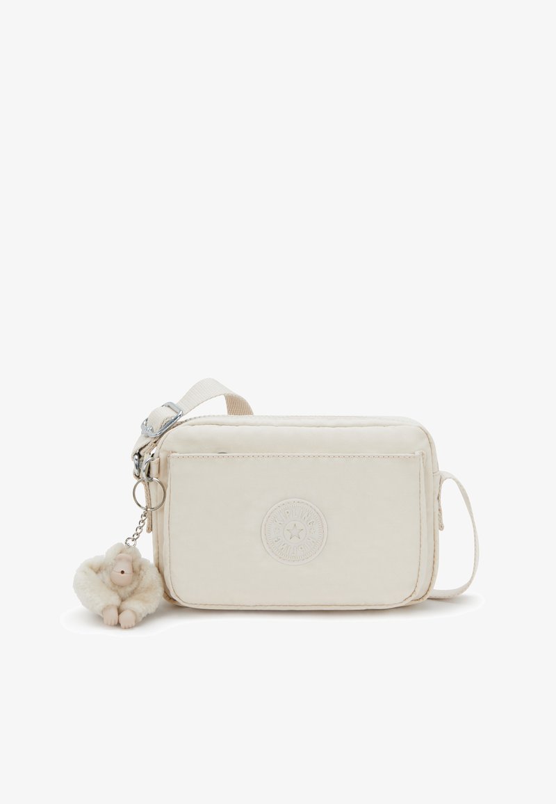 Kremowa torebka typu crossbody z teksturowanej tkaniny, z okrągłą naszywką z logo oraz puszystym charms do kluczy w kształcie małpki przymocowanym do srebrnego łańcuszka.