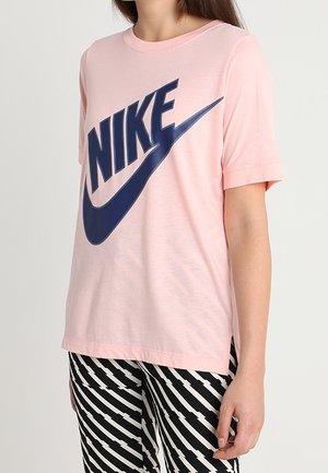 T-shirt en coton rose avec un grand logo Nike bleu marine. Manches courtes avec une coupe décontractée et des fentes latérales. Associé à un pantalon à rayures noires et blanches.