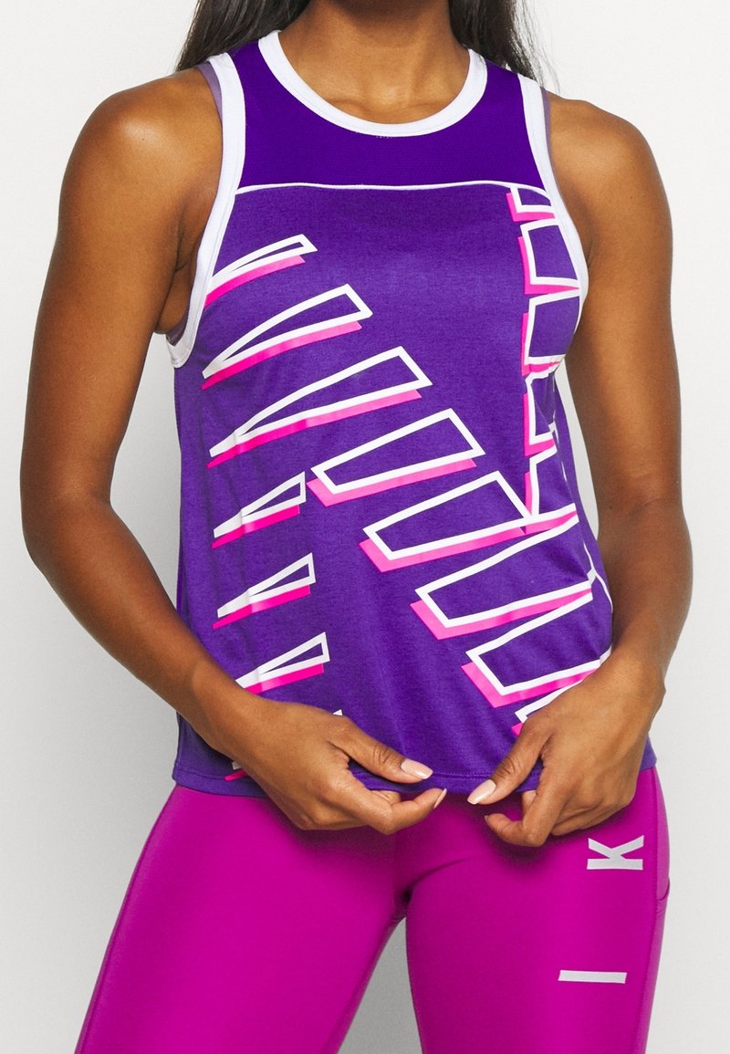 Fialové tílko s bílým a růžovým grafickým motivem, s kulatým výstřihem a sportovním střihem. Kombinováno s růžovými legínami.
