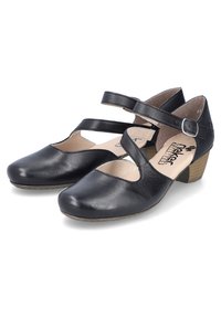 Chaussures noires en cuir de style Mary Jane avec deux brides croisées, petit talon en bois, bout arrondi et découpes sur les côtés.