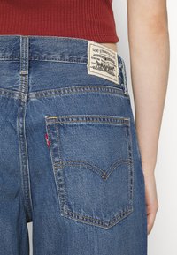 Modré denimové džíny s označením "Levi Strauss & Co." na pase. Mají dvě zadní kapsy s výraznými švy.