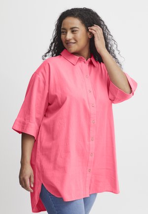 Chemise button-up rose surdimensionnée avec un col, des manches courtes et des fentes latérales. Fabriquée dans un tissu léger au toucher lisse.