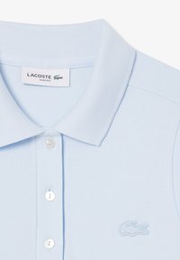 Svetlo modra Lacoste polo majica s slim fit krojem, ki ima teksturirano tkanino, dva gumbka in vezeno logo na prsih.
