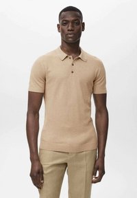 Polo a maniche corte beige con una trama testurizzata, colletto con tre bottoni e un design aderente. Abbinate a pantaloni beige chiaro.