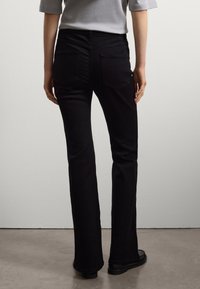 Jeans neri svasati con una texture liscia, due tasche posteriori e vita alta. Indossati con una maglietta grigia e scarpe nere.