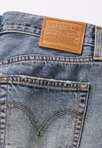 Jean en denim bleu avec patch en cuir signature Levi Strauss montrant le nom de la marque et les détails de la couture de la poche arrière.