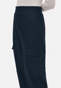 Pantalones cargo azul marino con una cintura ancha, bolsillos laterales y una textura suave, mostrados de lado.