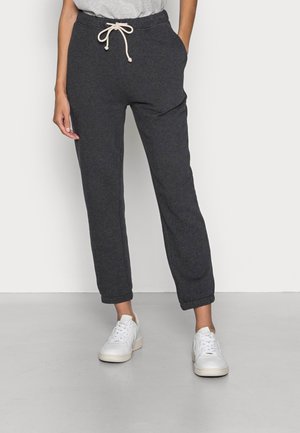 Person wearing dark gray sweatpants with drawstring waist and white sneakers, standing against a plain light background.