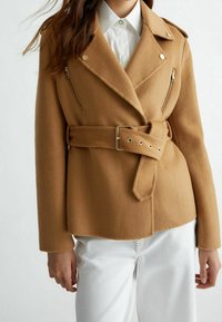 Kamelowa marynarka z mieszanki wełny o kroju dwurzędowym, z kieszeniami na zamek i paskiem w talii. Posiada wyłogi z wcięciem i miękką fakturę.