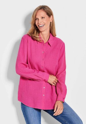 Fuchsia button-up shirt met een gestructureerde stof. Heeft lange mouwen, een puntige kraag en een ontspannen pasvorm, gecombineerd met blauwe jeans.