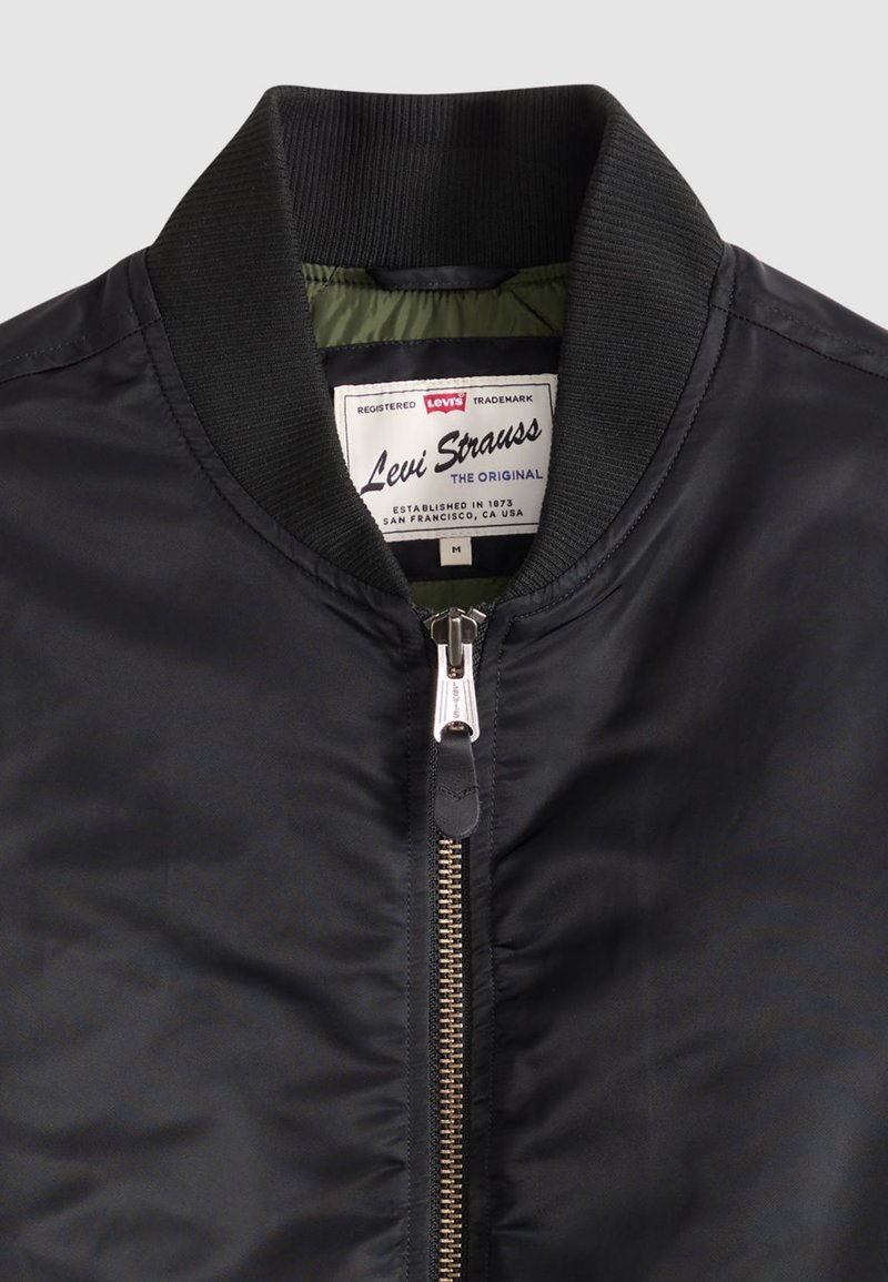 Giacca bomber nera Levi's con colletto a coste, cerniera argentata e fodera verde visibile all'interno del colletto.