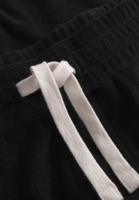 Black fabric with a soft texture, featuring a white drawstring tied in a knot, alongside visible ribbed elements.