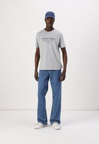 Grå bomulds t-shirt med "Tommy Hilfiger" logo, parret med blå denim cargo bukser og hvide sneakers. Accentueret med en lyseblå kasket.