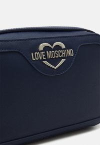 Námorně modrá texturovaná taška s stříbrným srdcovým logem a textem "LOVE MOSCHINO" na předním panelu.