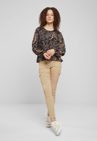 Blusa a maniche lunghe con un design a motivi scuri, abbinata a pantaloni cargo beige e sneakers bianche, con una vestibilità comoda e polsini elasticizzati.
