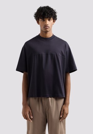 T-shirt a maniche corte, col girocollo, realizzato in tessuto uniforme di un profondo blu navy con una vestibilità rilassata. Presenta una sottile cucitura orizzontale sul petto.